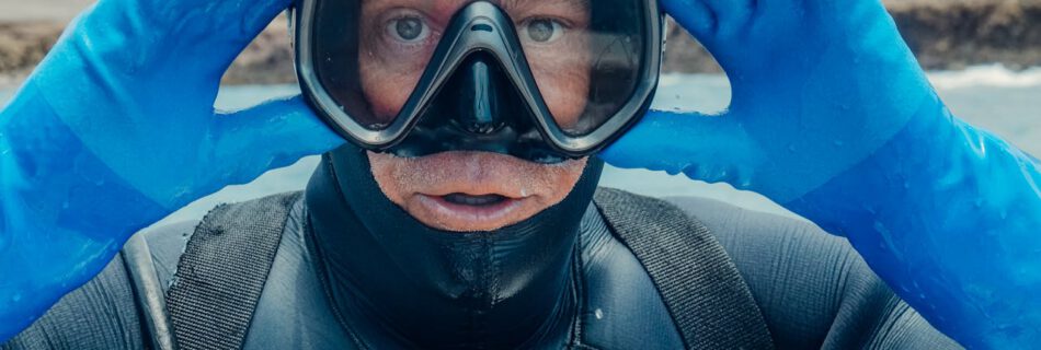 Taucher mit klarer Taucherbrille hält die Maske über Wasser. Wichtig immer Beschlagen der Taucherbrille vermeiden.