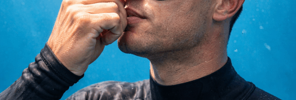 Freitaucher beim Druckausgleich (Valsalva-Methode) unter Wasser, Freediving, Taucher in schwarzem Neoprenanzug, klare Sicht, Luftblasen, natürliche Beleuchtung.